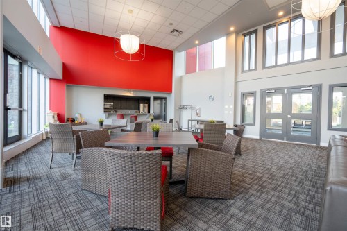 Community lounge featuring high ceilings, contemporary lighting fixtures, full-height windows, a kitchenette, and patterned carpet - #610 5151 Windermere Bv Sw, Edmonton, AB - Indoor
