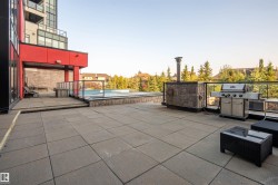 Expansive outdoor patio featuring large-format paver tiles, a stone-clad built-in grilling station, and a glass-paneled railing system - 