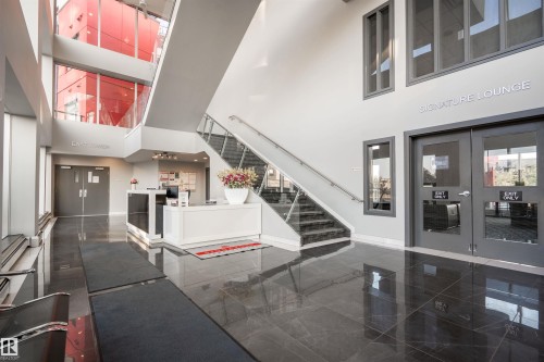 Spacious lobby with high ceilings, dark polished tile flooring, and a contemporary reception desk - #610 5151 Windermere Bv Sw, Edmonton, AB - Indoor Photo Showing Other Room