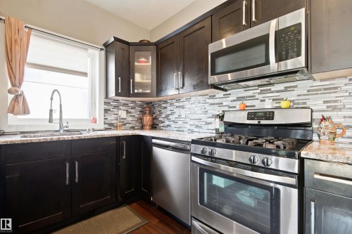 Dark-toned cabinetry with stainless steel hardware, granite-style countertops, stainless steel appliances, and a mosaic tile backsplash - 10833 63 Avenue Nw, Edmonton, AB 
