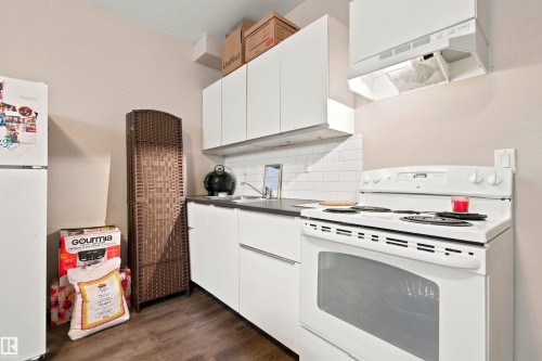 White cabinetry with modern hardware, dark countertops, white subway tile backsplash, stainless steel sink, and wood-finish flooring - 10833 63 Avenue Nw, Edmonton, AB 