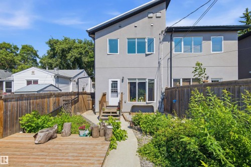 Rear exterior featuring contemporary gray siding, a wood deck, a concrete pathway, and a wood fence - 10833 63 Avenue Nw, Edmonton, AB 