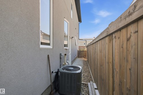 Stucco exterior wall with multiple windows, air conditioning unit, gravel landscaping, and wood privacy fencing - 10833 63 Avenue Nw, Edmonton, AB 