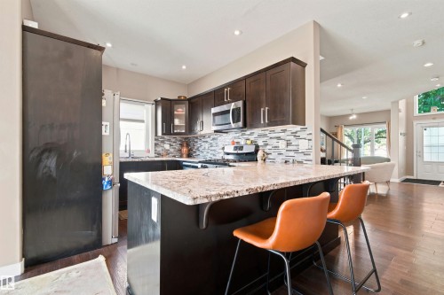 Kitchen featuring dark wood-finish cabinetry, stainless steel appliances, a mosaic tile backsplash, and a light-toned countertop island - 10833 63 Avenue Nw, Edmonton, AB 