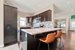 Kitchen featuring dark wood-finish cabinetry, stainless steel appliances, a mosaic tile backsplash, and a light-toned countertop island - 