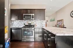 Kitchen featuring stainless steel appliances, dark wood-finish cabinetry, a patterned tile backsplash, light-colored stone countertops, and recessed lighting - 