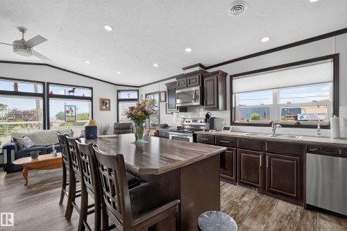Kitchen featuring a central island with bar seating, dark wood-finish cabinetry, stainless steel appliances, and wood-finish flooring - 4204 47 Street, Wetaskiwin, AB - Indoor