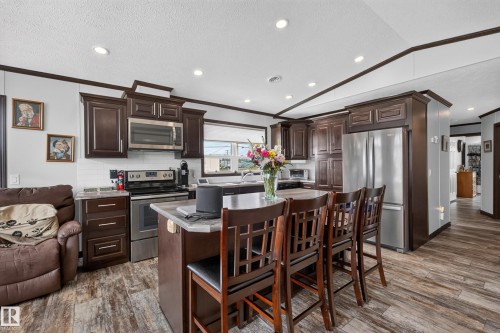Spacious kitchen featuring dark wood cabinetry, stainless steel appliances, a center island with bar seating, recessed lighting, and wood-finish flooring - 4204 47 Street, Wetaskiwin, AB - Indoor Photo Showing Other Room