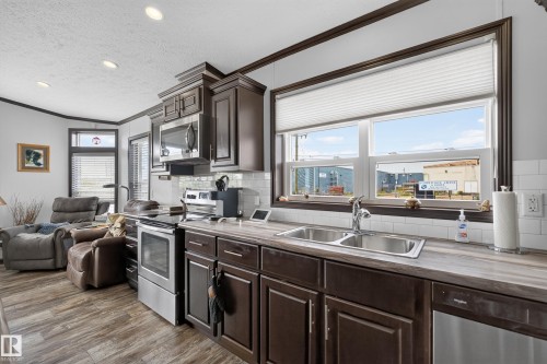 Modern kitchen featuring wood-finish flooring, stainless steel appliances, dark wood cabinetry, a subway tile backsplash, and a double basin sink - 4204 47 Street, Wetaskiwin, AB - Indoor Photo Showing Kitchen With Double Sink