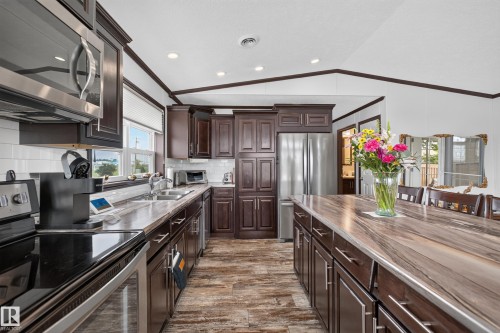 Spacious kitchen featuring dark wood cabinetry, stainless steel appliances, a large center island, wood-finish flooring, and recessed lighting - 4204 47 Street, Wetaskiwin, AB - Indoor Photo Showing Kitchen With Stainless Steel Kitchen With Double Sink