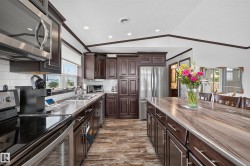 Spacious kitchen featuring dark wood cabinetry, stainless steel appliances, a large center island, wood-finish flooring, and recessed lighting - 