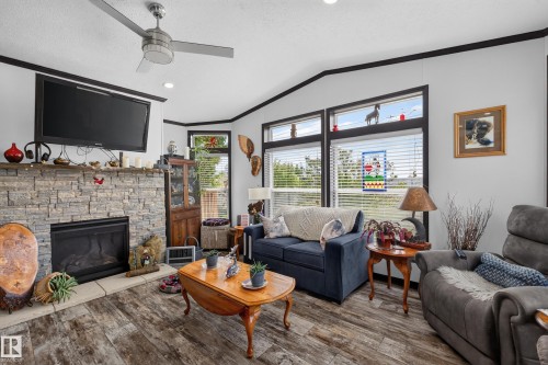 Living area featuring a stone-clad fireplace with a hearth, wood-finish flooring, and multiple windows with blinds - 4204 47 Street, Wetaskiwin, AB - Indoor Photo Showing Living Room With Fireplace