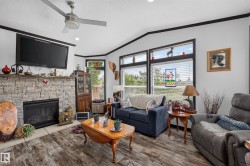 Living area featuring a stone-clad fireplace with a hearth, wood-finish flooring, and multiple windows with blinds - 