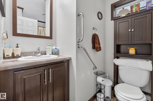 Bathroom featuring a dark wood-finish vanity with an integrated sink, coordinating wall-mounted mirror, and an over-toilet storage cabinet - 4204 47 Street, Wetaskiwin, AB - Indoor Photo Showing Bathroom