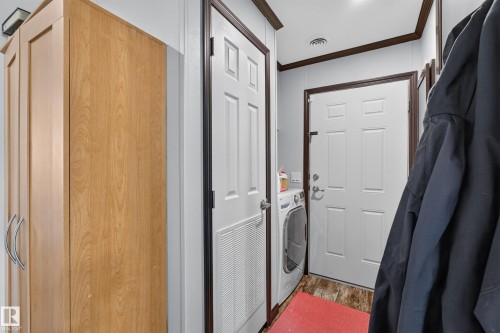 Utility area featuring a wood-finish storage cabinet with curved chrome handles, a white paneled door with a vent, and a second white paneled door - 4204 47 Street, Wetaskiwin, AB - Indoor Photo Showing Laundry Room