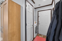 Utility area featuring a wood-finish storage cabinet with curved chrome handles, a white paneled door with a vent, and a second white paneled door - 