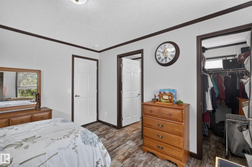 Bedroom featuring light gray walls with dark trim, wood-finish flooring, a white paneled door, and a closet with an integrated window - 4204 47 Street, Wetaskiwin, AB - Indoor Photo Showing Bedroom