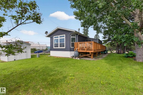 Expansive rear yard featuring a large wood deck, mature trees, a storage shed, and dark siding with white trim - 4204 47 Street, Wetaskiwin, AB - Outdoor With Deck Patio Veranda