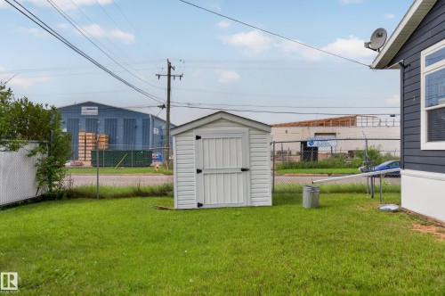 Manicured lawn featuring a white vinyl storage shed with black hardware, complementing the dark gray siding and white trim of the main structure - 4204 47 Street, Wetaskiwin, AB - Outdoor