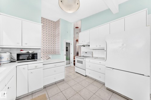 Kitchen featuring white cabinetry, integrated white appliances, tile flooring, and a tile backsplash - 3311 104 Avenue Nw, Edmonton, AB 