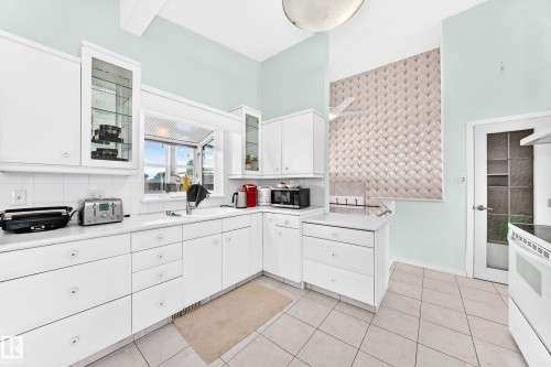 White cabinetry with glass-front upper cabinets, white countertop, tile flooring, and a patterned accent wall - 3311 104 Avenue Nw, Edmonton, AB 
