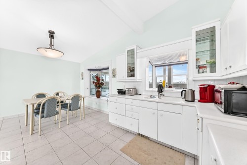 White cabinetry with glass-front upper cabinets, light-colored tile flooring, vaulted ceiling, and a large bay window - 3311 104 Avenue Nw, Edmonton, AB 