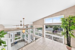 Vaulted ceiling, ceiling-mounted light fixtures, tiled flooring, expansive windows, and a glass-paneled railing - 