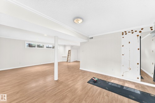 Spacious room featuring wood-finish flooring, white crown molding, and recessed lighting - 3311 104 Avenue Nw, Edmonton, AB 