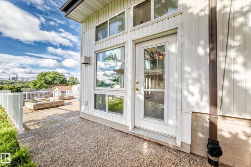 Modern farmhouse exterior featuring clean white vertical siding, expansive glass doors and windows with white framing, and a gravel patio area - 3311 104 Avenue Nw, Edmonton, AB 