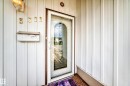 White siding exterior with a storm door featuring an arched glass insert, traditional wall-mounted light fixture, and brass house numbers - 3311 104 Avenue Nw, Edmonton, AB 