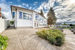 White exterior with multiple windows, glass-paneled double doors, and a decorative concrete patio - 