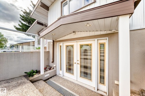 Covered entry with dual glass-paneled doors, recessed lighting, and a glass-paneled railing - 3311 104 Avenue Nw, Edmonton, AB 