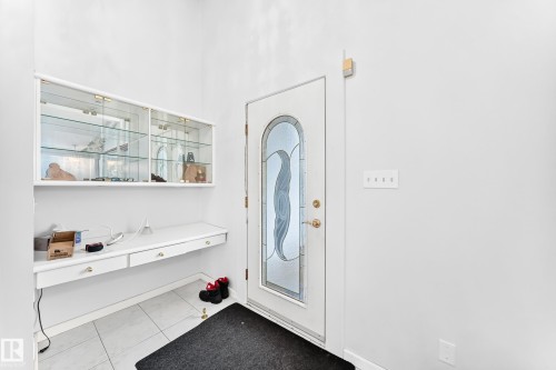 White entry door with decorative glass insert, white floating desk with drawers, white wall-mounted display cabinetry with glass doors, and light-toned tile flooring - 3311 104 Avenue Nw, Edmonton, AB 
