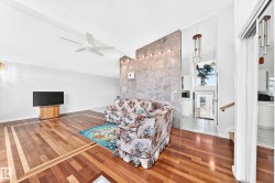 Vaulted ceiling with a ceiling fan, wood-finish flooring with inlay details, and a stone accent wall with integrated lighting - 