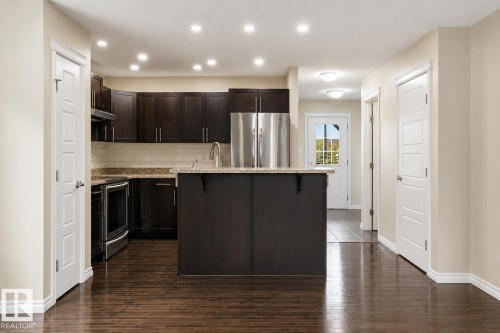 Kitchen featuring dark wood-finish cabinetry, stainless steel appliances, a tiled backsplash, a central island with a countertop, and recessed lighting - 445 Watt Boulevard Sw, Edmonton, AB 