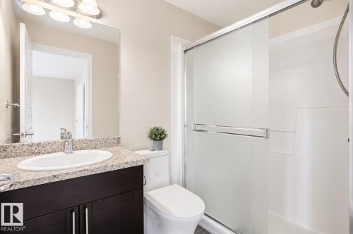 Bathroom featuring a vanity with an oval sink, dark wood-finish cabinetry, a stone-finish countertop, and a shower with frosted glass sliding doors - 445 Watt Boulevard Sw, Edmonton, AB 