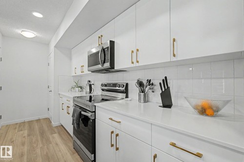 Contemporary kitchen featuring white flat-panel cabinetry with gold-tone hardware, white countertops, and a white subway tile backsplash - #12 905 172 St Sw, Edmonton, AB - Indoor Photo Showing Kitchen With Upgraded Kitchen