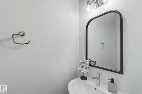 White pedestal sink with a chrome single-handle faucet, complemented by an arched black-framed mirror - #12 905 172 St Sw, Edmonton, AB - Indoor Photo Showing Bathroom