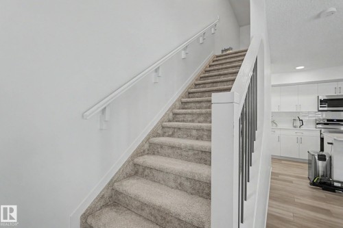 Carpeted staircase with white handrail and modern black metal balusters - #12 905 172 St Sw, Edmonton, AB - Indoor