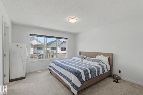 Bedroom featuring a large window with white trim, neutral-toned walls, and soft carpeting - #12 905 172 St Sw, Edmonton, AB - Indoor Photo Showing Bedroom