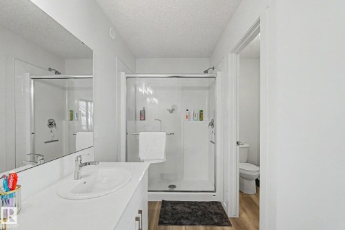 Bathroom featuring a contemporary shower with glass enclosure, single vanity with integrated sink, chrome faucet, and wood-finish flooring - #12 905 172 St Sw, Edmonton, AB - Indoor Photo Showing Bathroom
