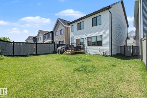Expansive grassy yard featuring a wood privacy fence with black trim, a rear deck with dark railing, and a vinyl-sided exterior with black-framed windows - #12 905 172 St Sw, Edmonton, AB - Outdoor