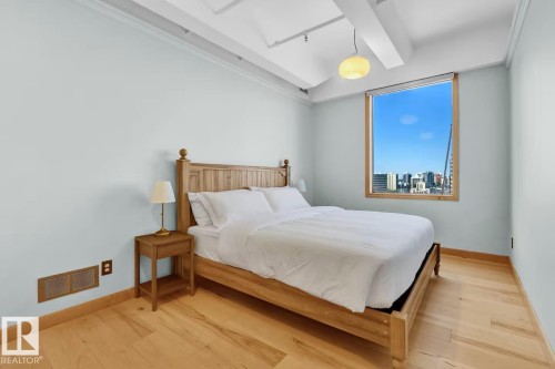 Light wood-finish flooring with coordinating wood trim, large window with wood framing, and exposed ceiling beams - #903 10105 109 St Nw, Edmonton, AB 