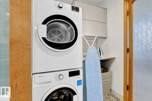 Stacked front-load washer and dryer, light wood-finish cabinetry, light blue subway tile, textured glass door, and built-in upper cabinetry - #903 10105 109 St Nw, Edmonton, AB 