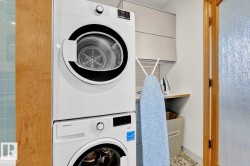 Stacked front-load washer and dryer, light wood-finish cabinetry, light blue subway tile, textured glass door, and built-in upper cabinetry - 