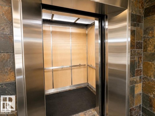 Elevator access featuring brushed stainless steel framing, wood-finish interior panels, and a textured floor mat - #903 10105 109 St Nw, Edmonton, AB 