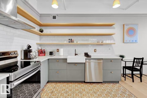 Kitchen featuring a subway tile backsplash, open wood-finish shelving, stainless steel appliances, and patterned floor tile - #903 10105 109 St Nw, Edmonton, AB 