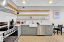 Kitchen featuring a subway tile backsplash, open wood-finish shelving, stainless steel appliances, and patterned floor tile - #903 10105 109 St Nw, Edmonton, AB 