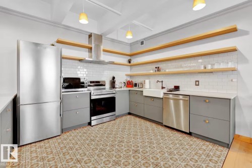 Kitchen featuring stainless steel appliances, open wood shelving, gray cabinetry, subway tile backsplash, and patterned floor tile - #903 10105 109 St Nw, Edmonton, AB 