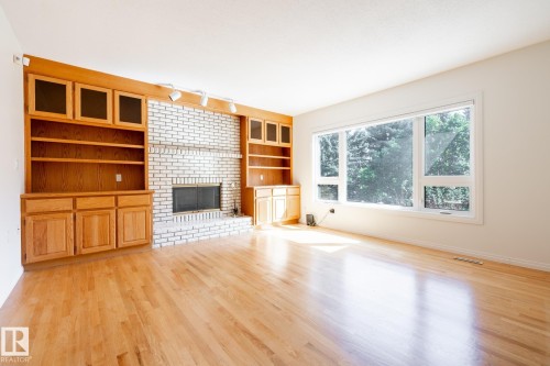 Light wood-finish flooring, built-in wooden cabinetry, white brick fireplace, large windows, and track lighting - 14 Highlands Place, Wetaskiwin, AB 